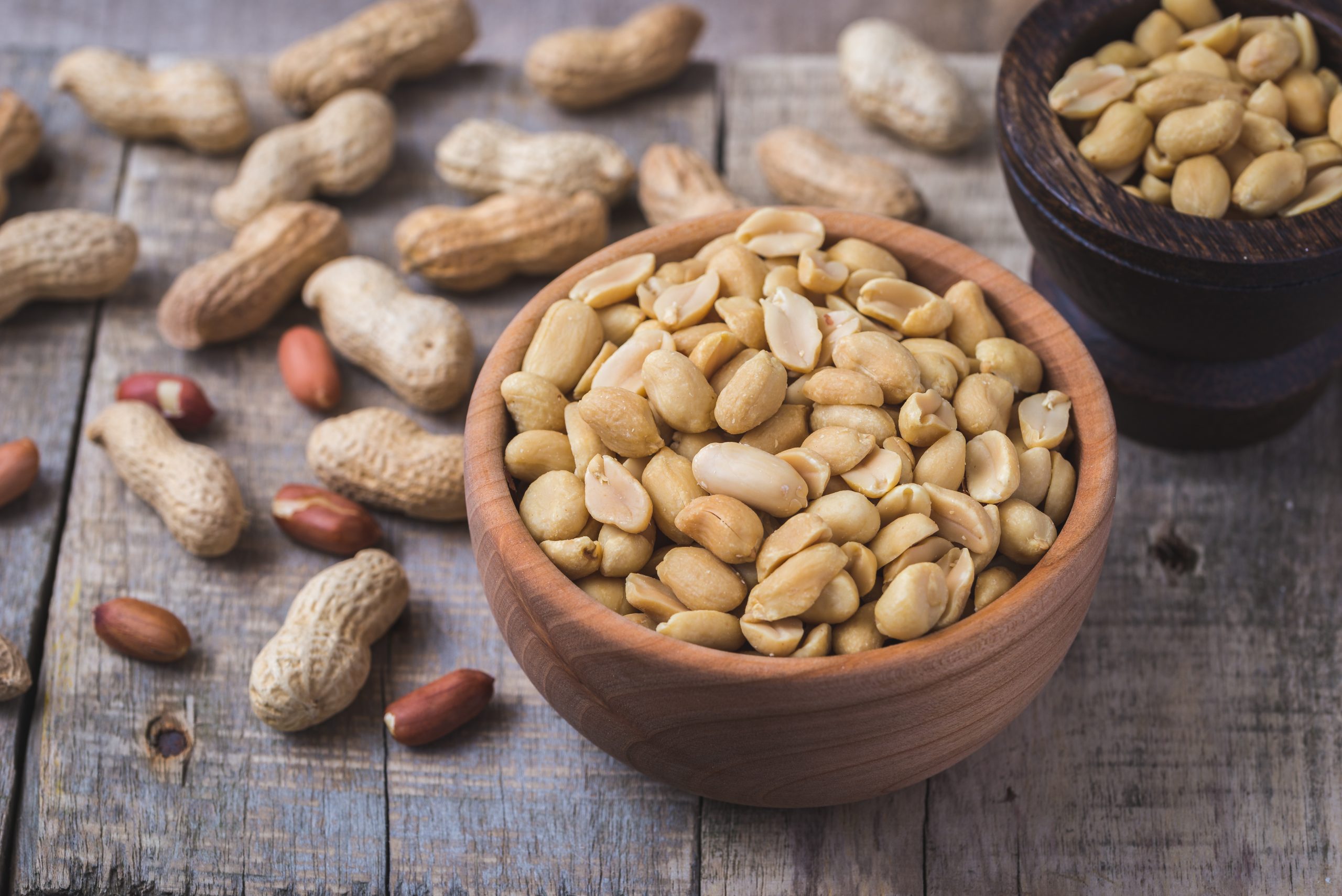 Peanuts in small wooden bowl on natural rustic desk.